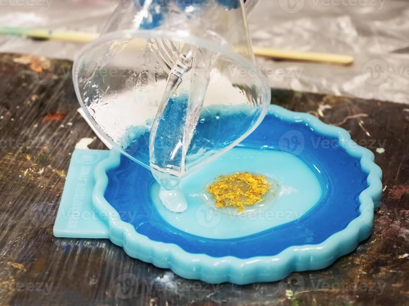 The art process of pouring epoxy resin into a golden toy. Technology process of creating a painting in style resin art, works with epoxy in studio, makes a wooden stand with the image. Close up. photo