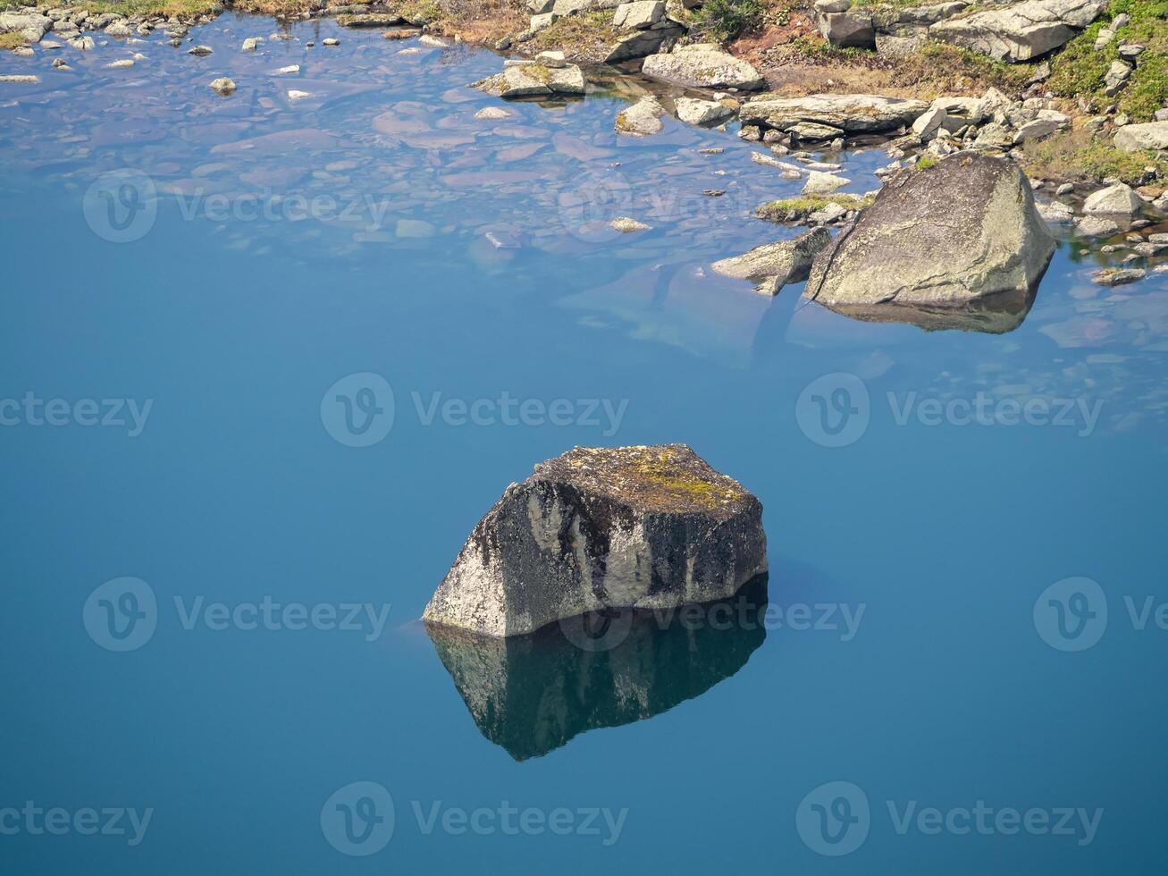 Stone reflection in still clear blue water. photo