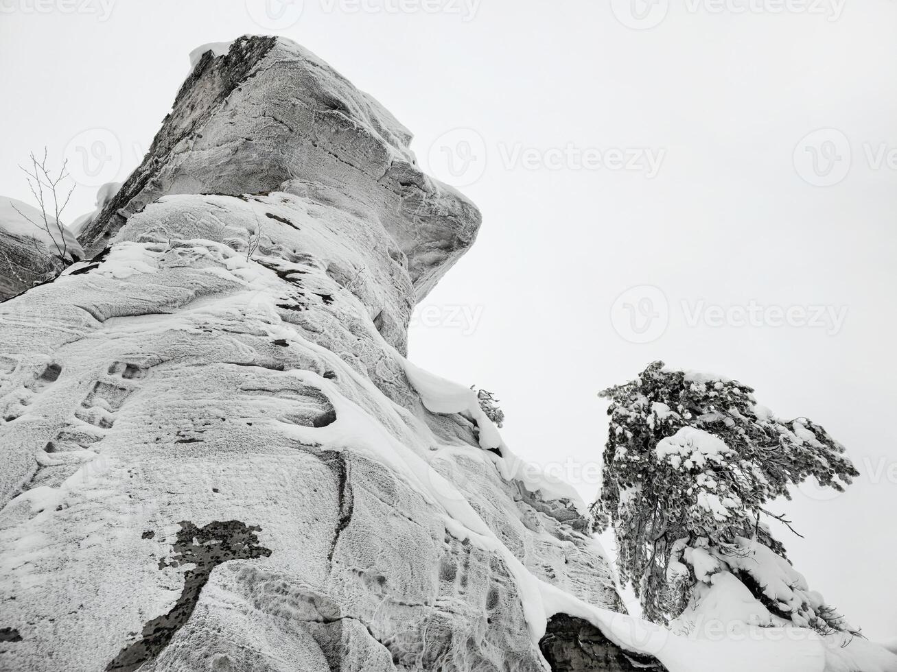 Large stone cliff covered with frozen snow, view from below. photo