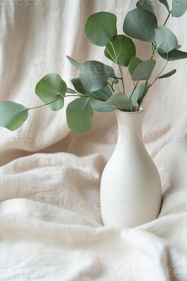 Styled display features a matte white ceramic bottle filled with fresh eucalyptus leaves, elegantly placed on soft beige linen fabric, providing ample space for text overlay and branding photo