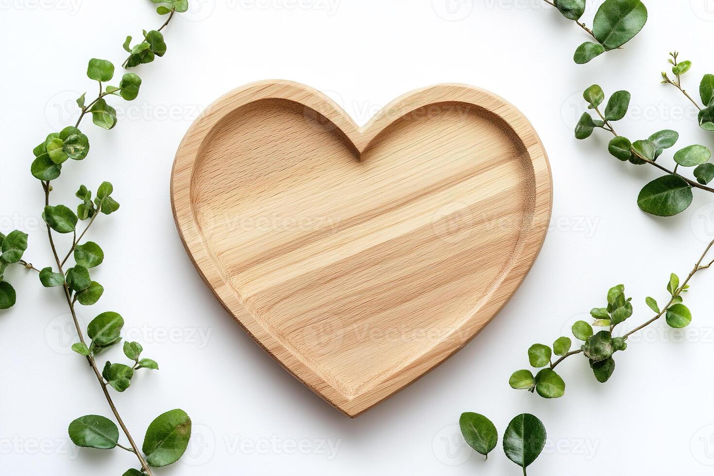 A heart-shaped plate made of light oak wood rests on a smooth white surface, accented by small green leaves. The ample negative space invites personalization or text overlay photo