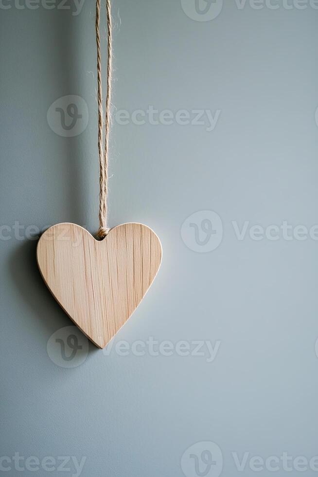 A handmade wooden heart ornament is gracefully suspended on a simple cord against a soft, neutral backdrop. This minimalist setting enhances the stylish design, providing space for text photo