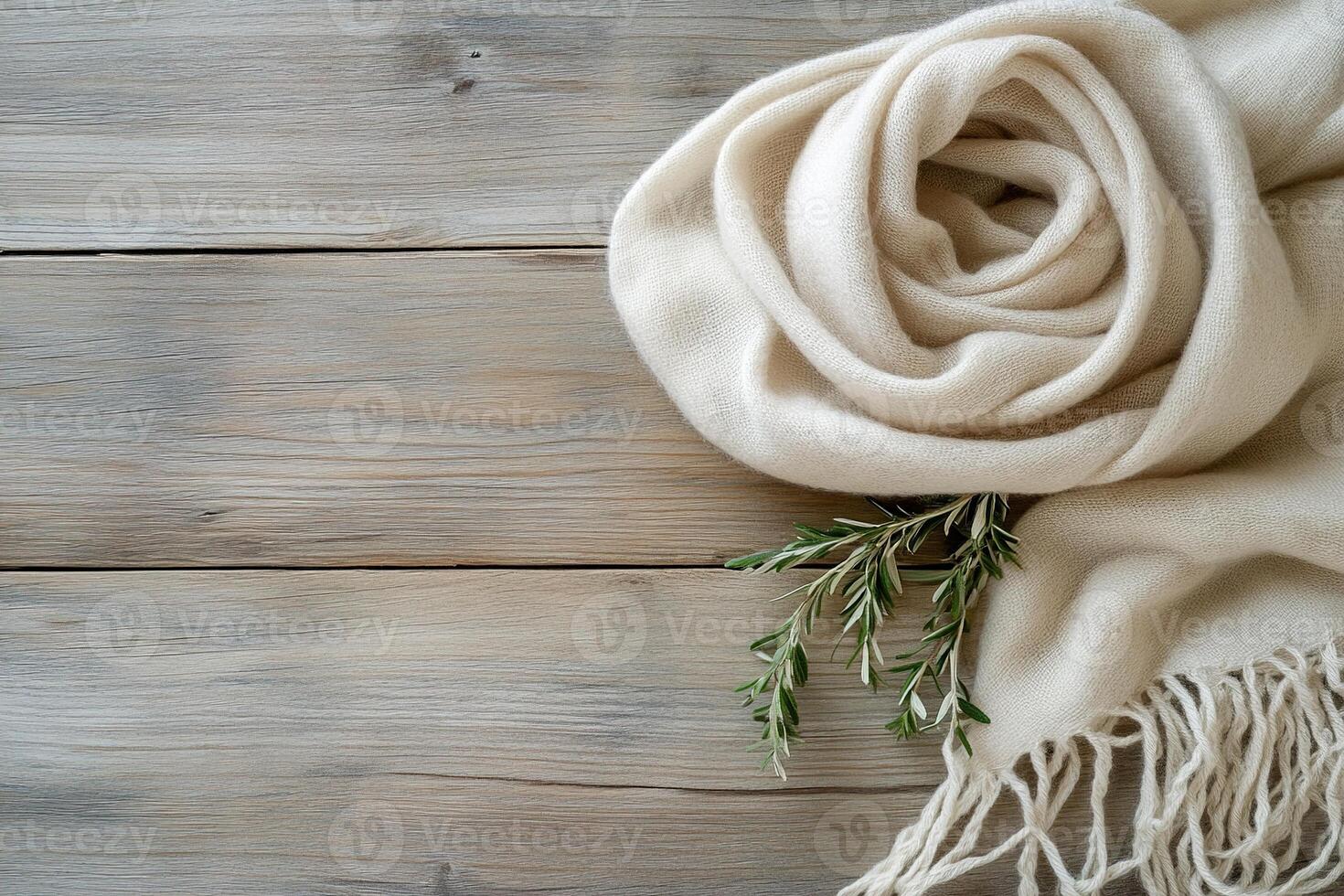 A soft wool scarf in light taupe is gently draped over a clean wooden surface, accompanied by a small sprig of greenery for a calming and organic touch, ideal for a cozy setting photo