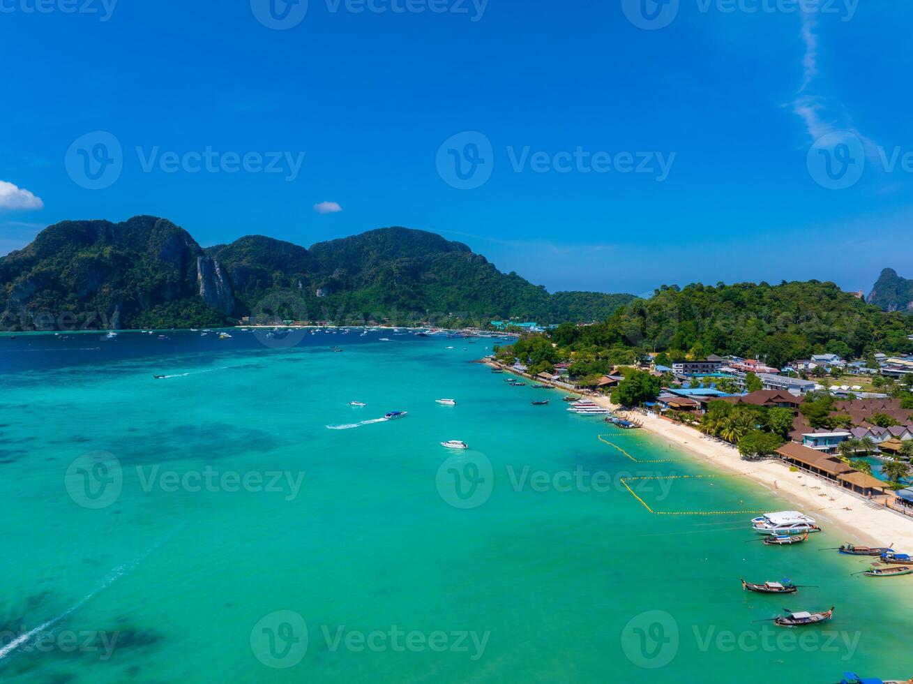 Aerial view of a tropical beach on Phi Phi Islands, Thailand, with turquoise waters, small boats, white sand, lush greenery, and limestone hills. photo