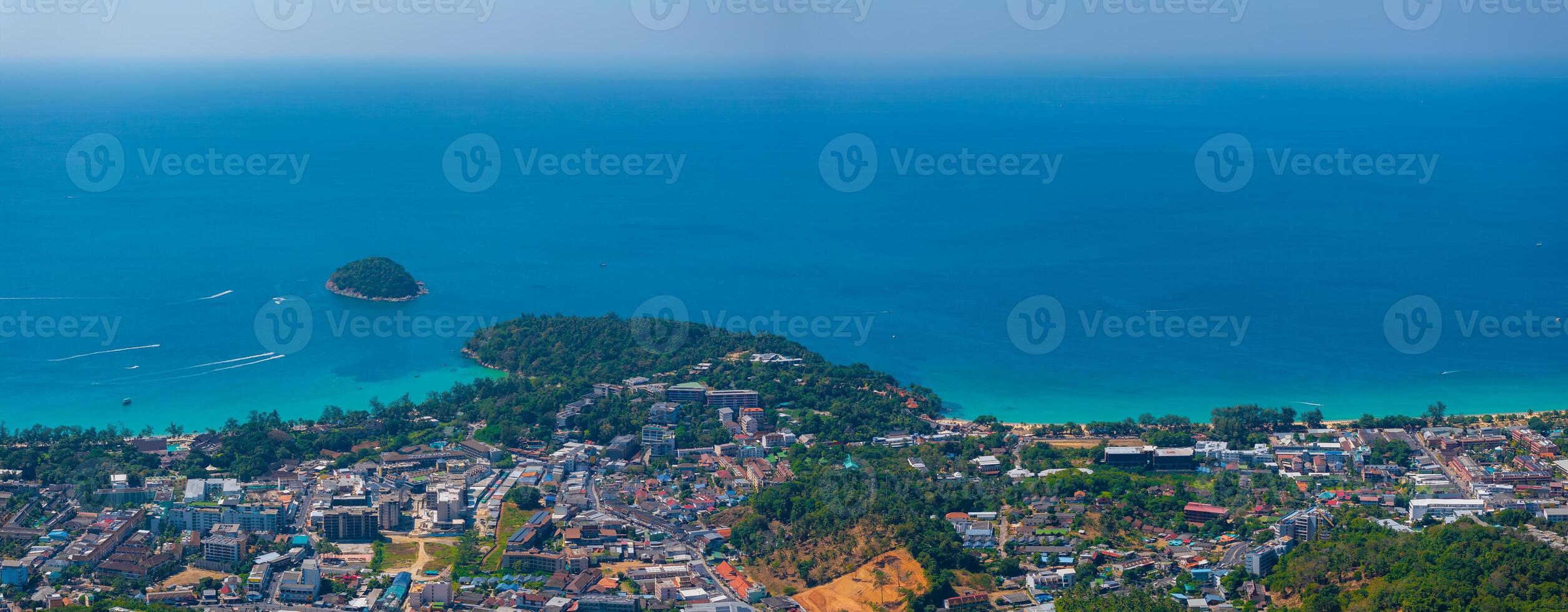 Aerial view of a coastal town in Phuket, Thailand, with turquoise waters, a lush offshore island, and a mix of urban and natural landscapes. photo