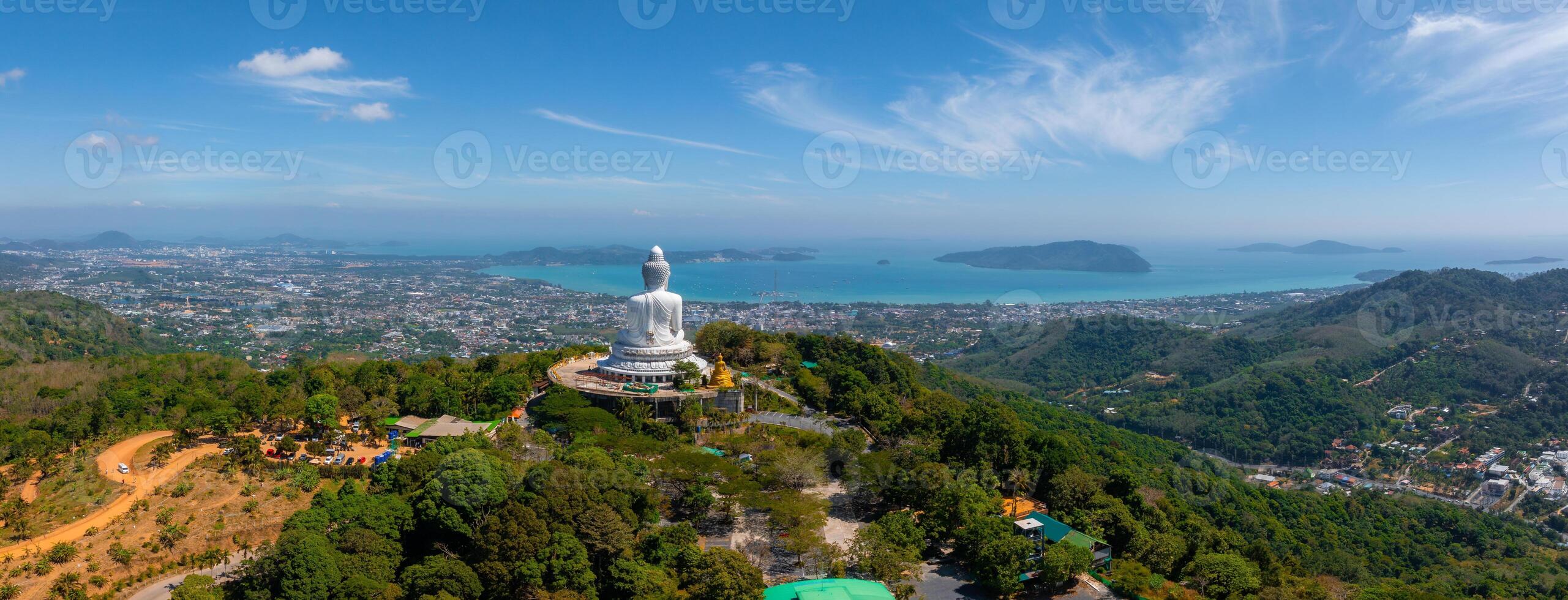 Aerial perspective of the Big Buddha statue in Phuket, Thailand, atop a green hill with views of the city, Andaman Sea, islands, and clear skies. photo
