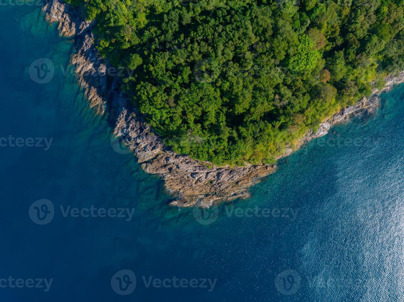 Aerial perspective of a lush, green forested coastline on a rocky peninsula surrounded by vibrant blue waters, likely in Phuket or Phi Phi Islands. photo