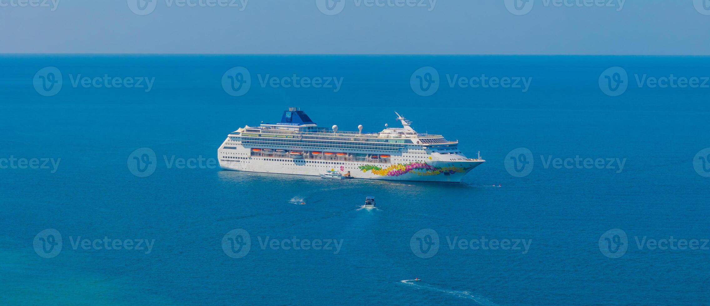A vibrant cruise ship with colorful designs sails in clear blue waters, accompanied by smaller boats under a bright, cloudless sky near Phuket or Phi Phi Islands. photo