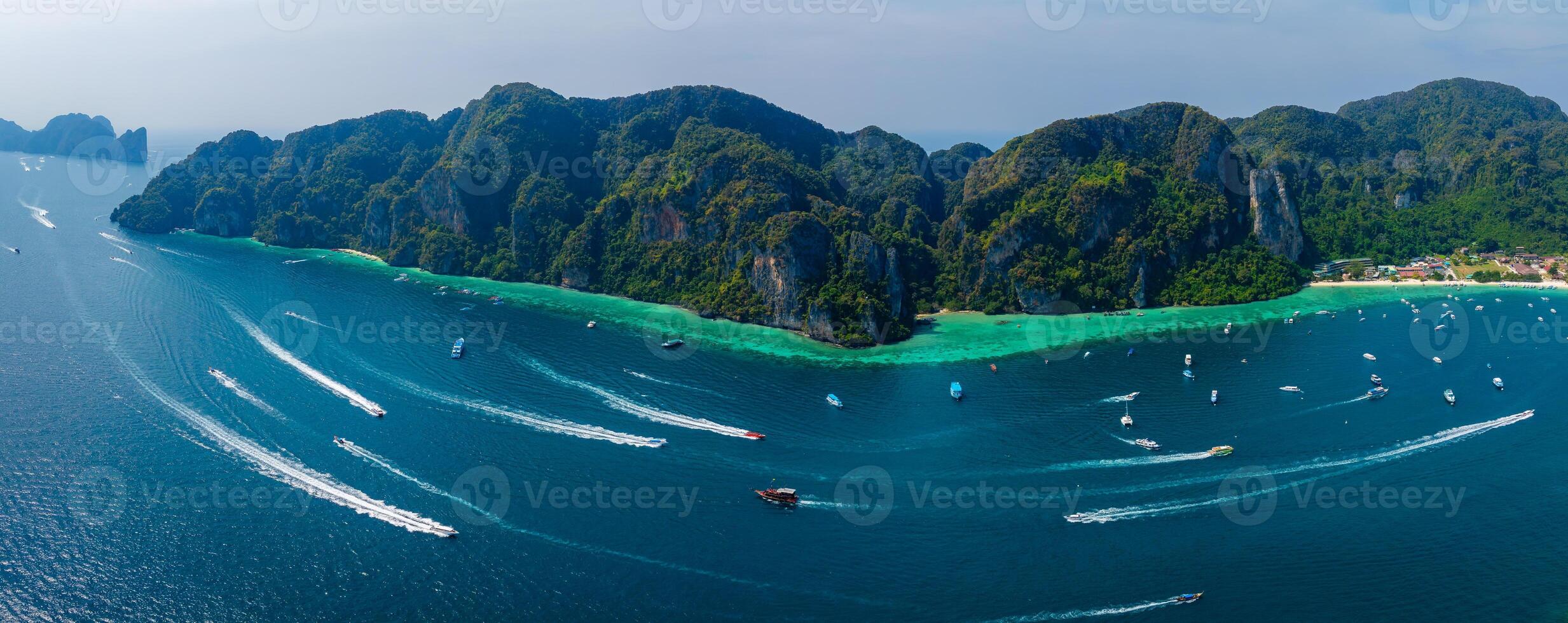 Aerial perspective of Phi Phi Islands, Thailand, showing green cliffs, turquoise waters, boats, yachts, and a small settlement along the coast. photo