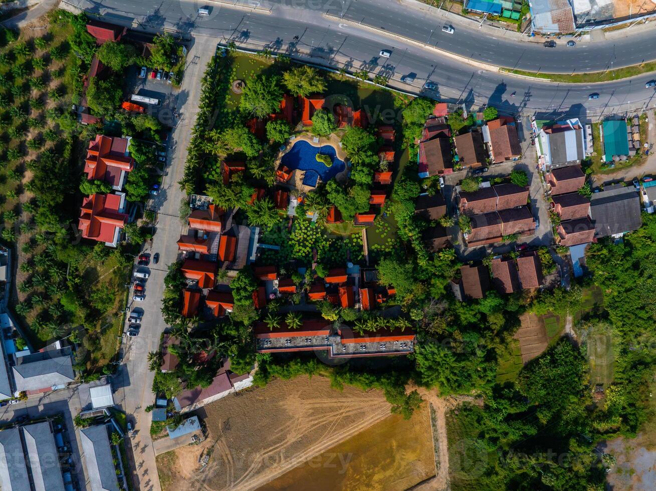 Aerial image of a red roofed building complex with a blue pool, surrounded by greenery, roads, and residential areas in Phuket, Thailand. photo