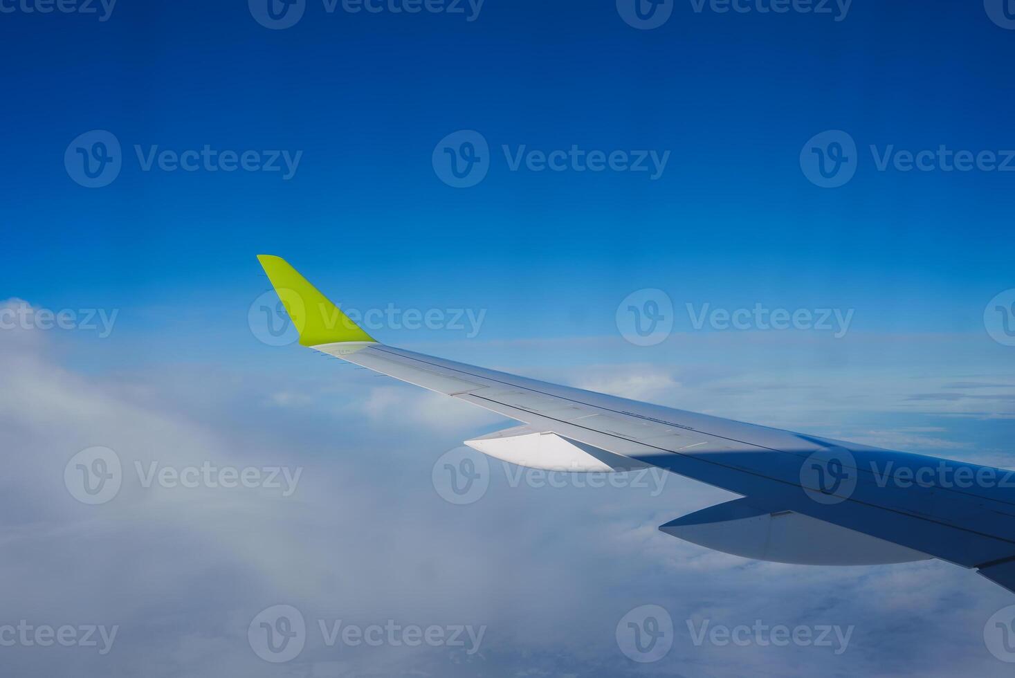 Airplane Wing with Green Wingtip Against Clear Blue Sky Mid Flight photo