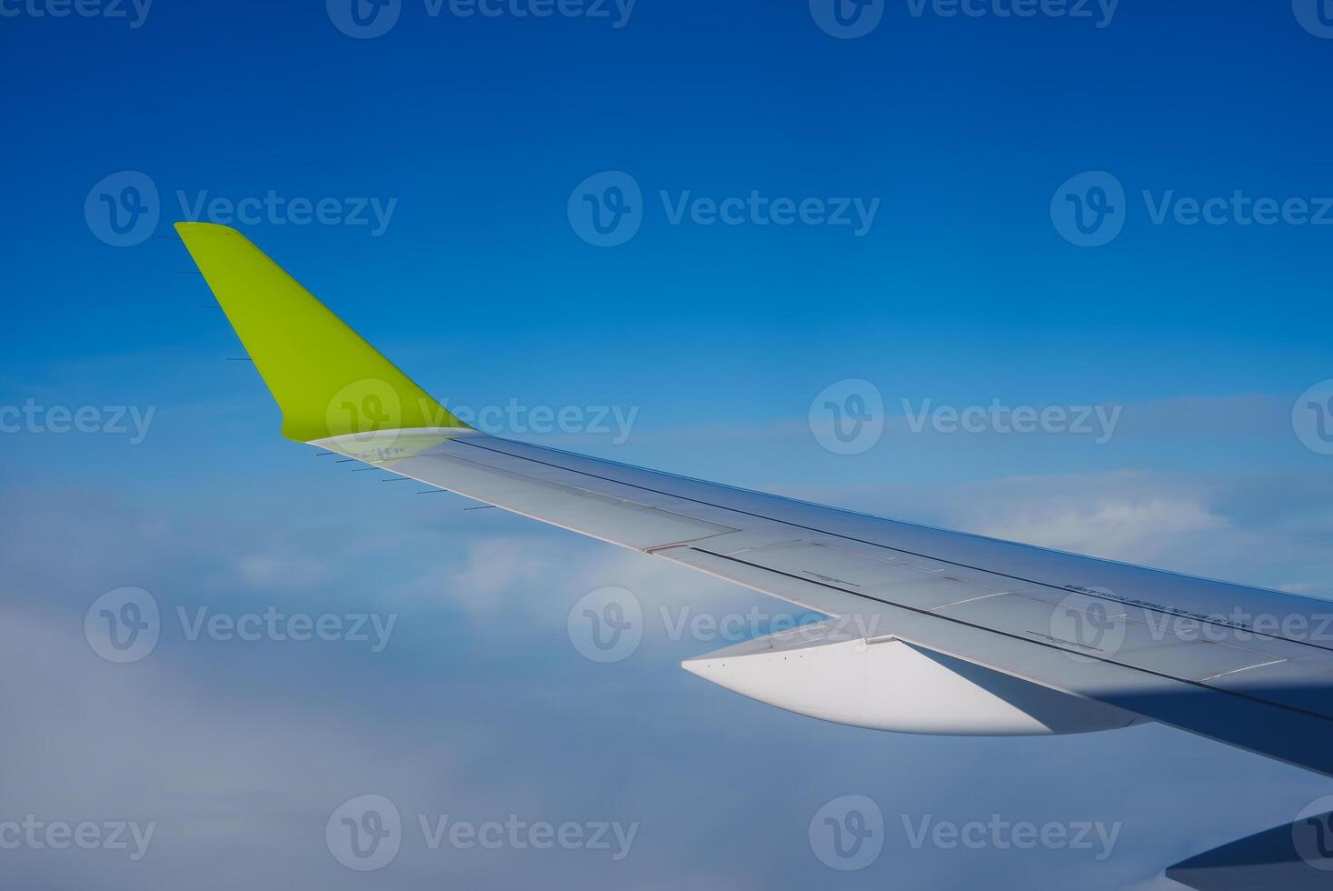 Airplane Wing with Bright Green Wingtip Against Blue Sky and Clouds photo