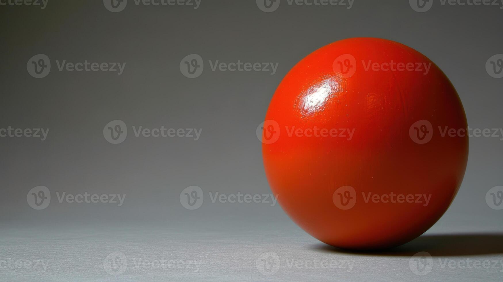 A solitary red sphere rests on a gray surface photo