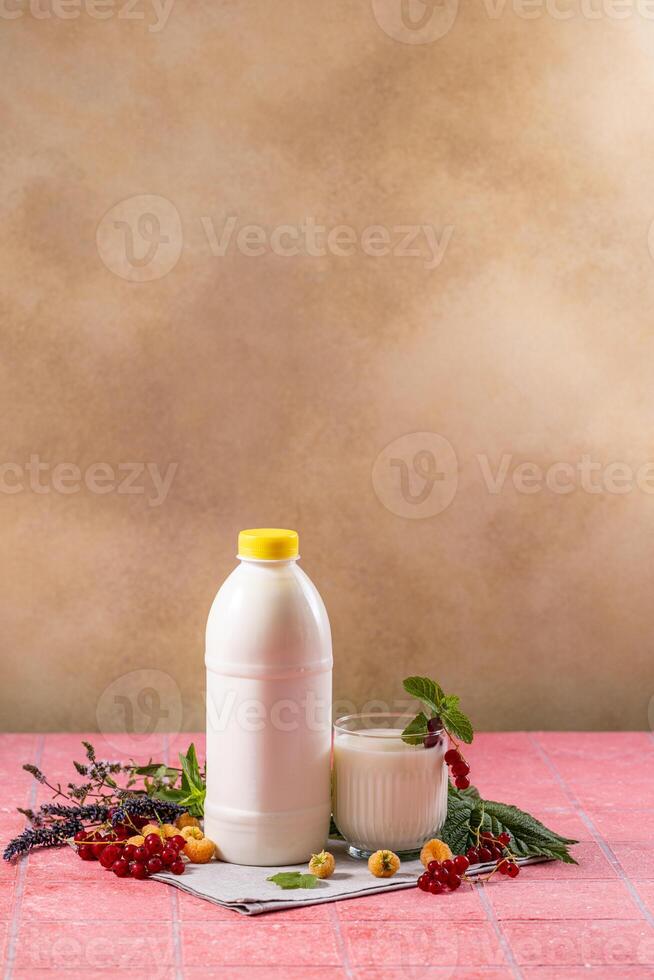 Yogurt or kefir in bottle and glass with red and yellow berries, mint and lavender on pink tile table photo