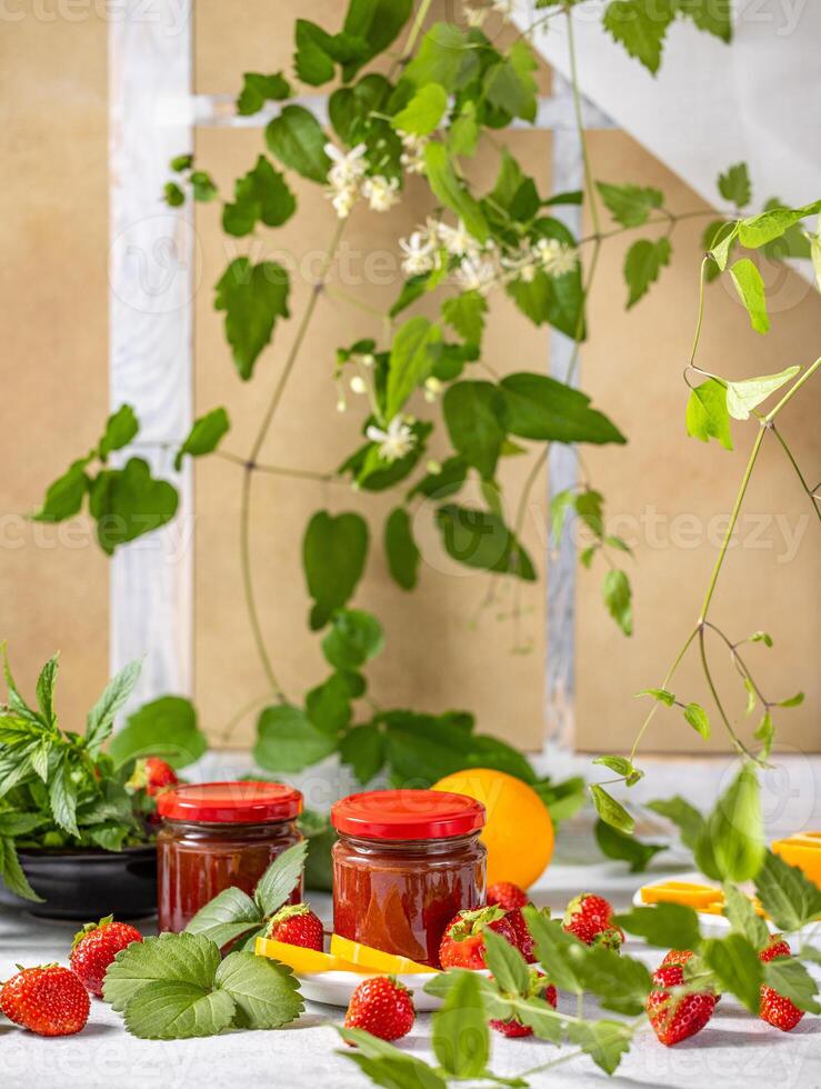 Jars of strawberry jam with fresh strawberries and orange slices photo