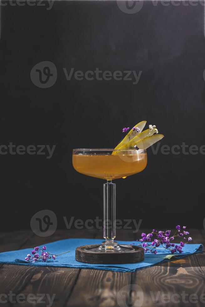 Elegant coupe glass with pear and flower garnish on dark wooden table photo