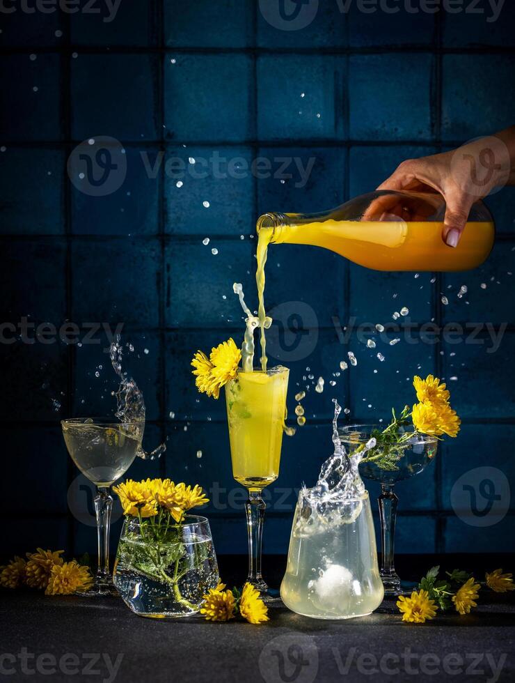 Bartender pouring yellow cocktail into glasses with ice and flowers, splashing liquid photo