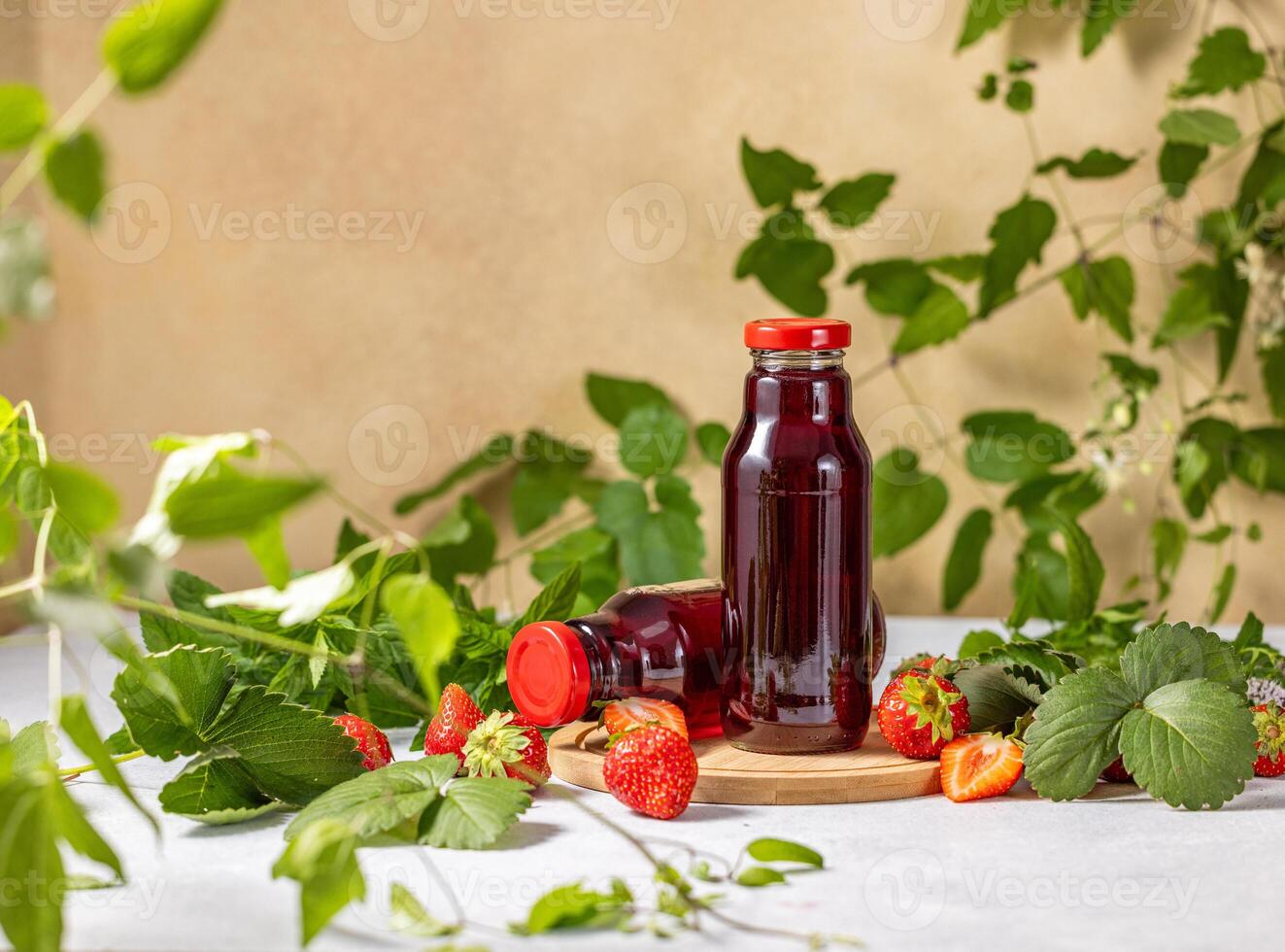 Fresh strawberry juice in glass bottles surrounded by strawberry leaves photo