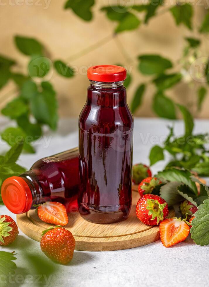 Two strawberry juice bottles standing on wooden board with fresh strawberries and leaves photo