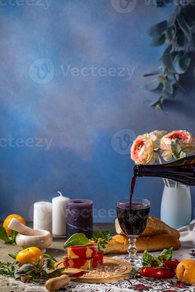 Pouring red wine into glass with gourmet cheese, bread, and fruits on table photo