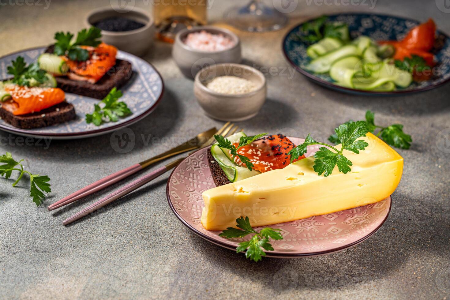 Wedge of cheese with sandwiches topped with smoked salmon and cucumber on gray table photo