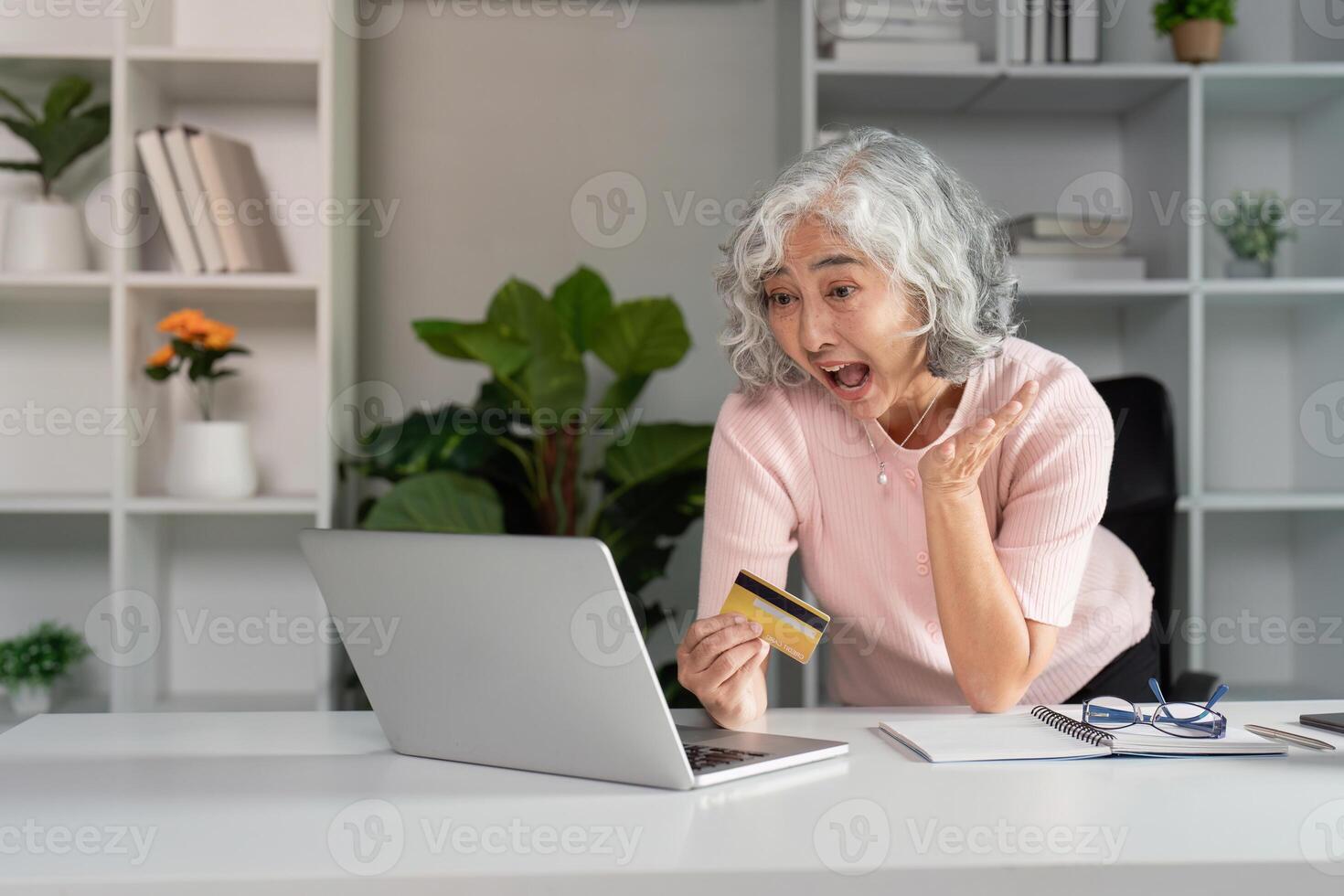 Surprised elderly woman expressing excitement while shopping online with a credit card in a modern home office photo