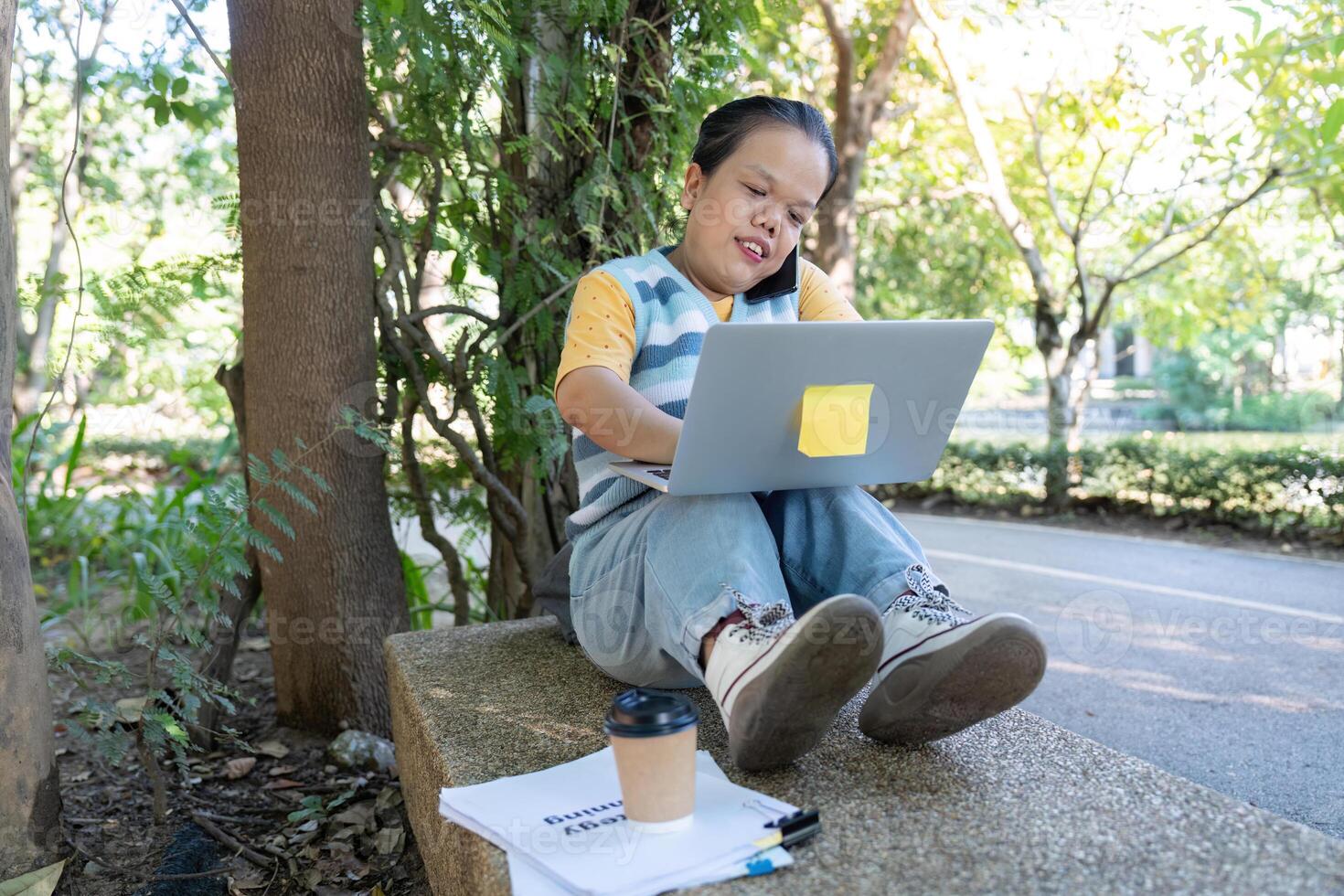 Woman with achondroplasia working on a laptop with coffee in a tranquil park photo