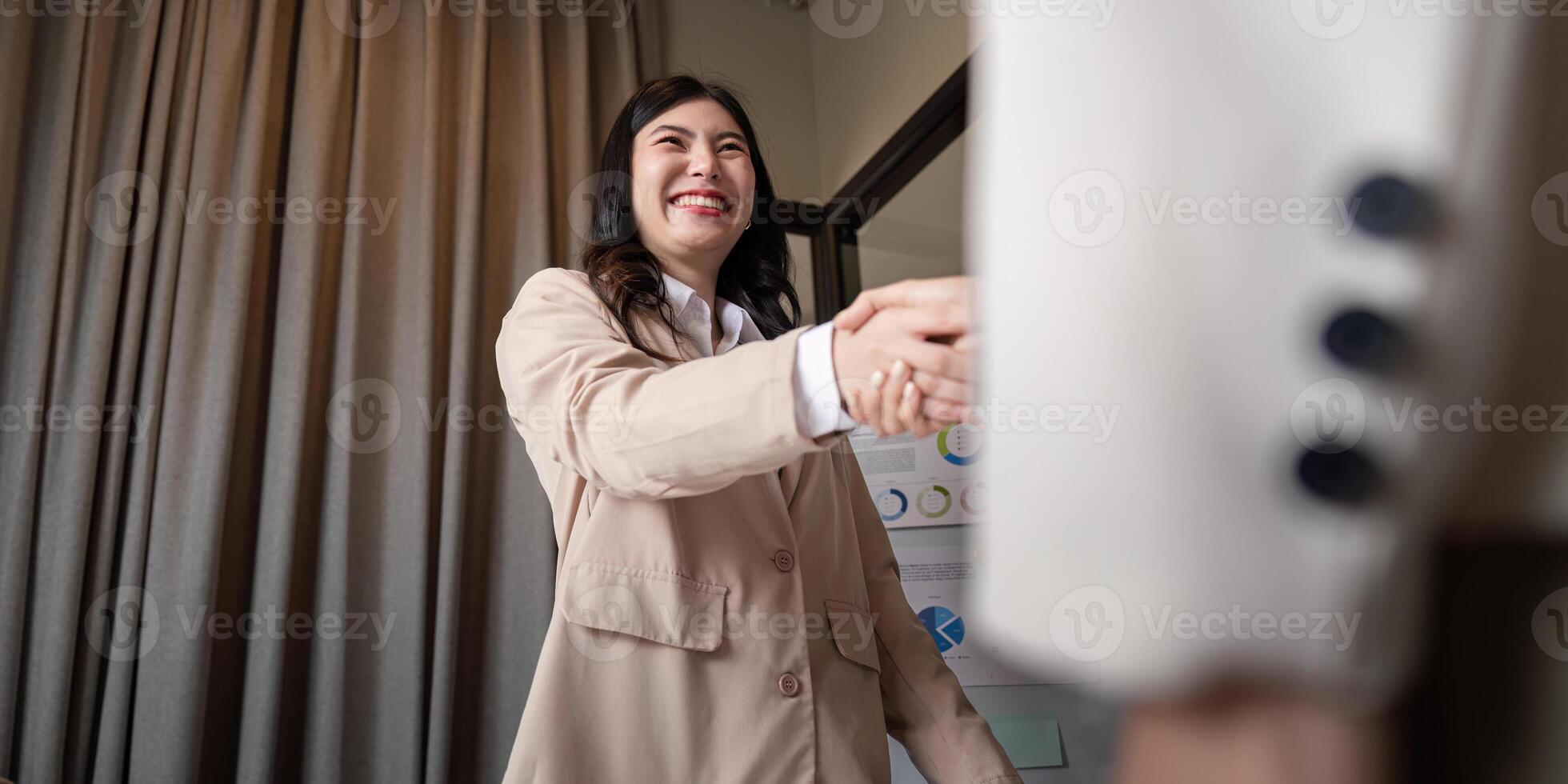 Joyful female professional smiling while shaking hands to finalize a business agreement in modern office photo