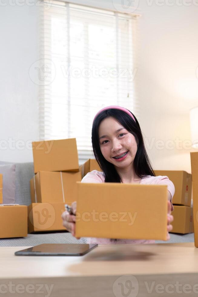 Young female entrepreneur showcasing a package while managing her e-commerce business from home photo