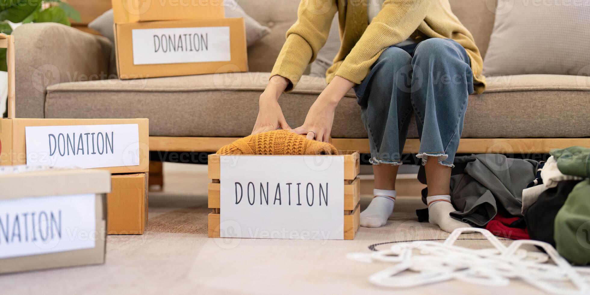 Woman gently placing a knitted sweater into a donation box, organizing clothes in a warm living room photo
