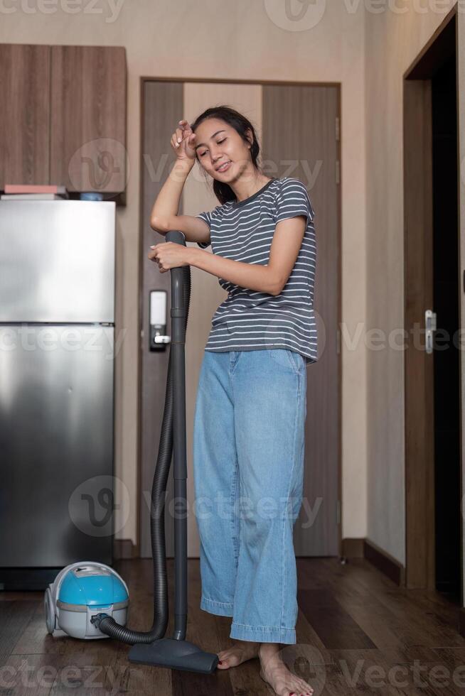Tired young woman taking a break while vacuuming her kitchen, looking relaxed and content photo