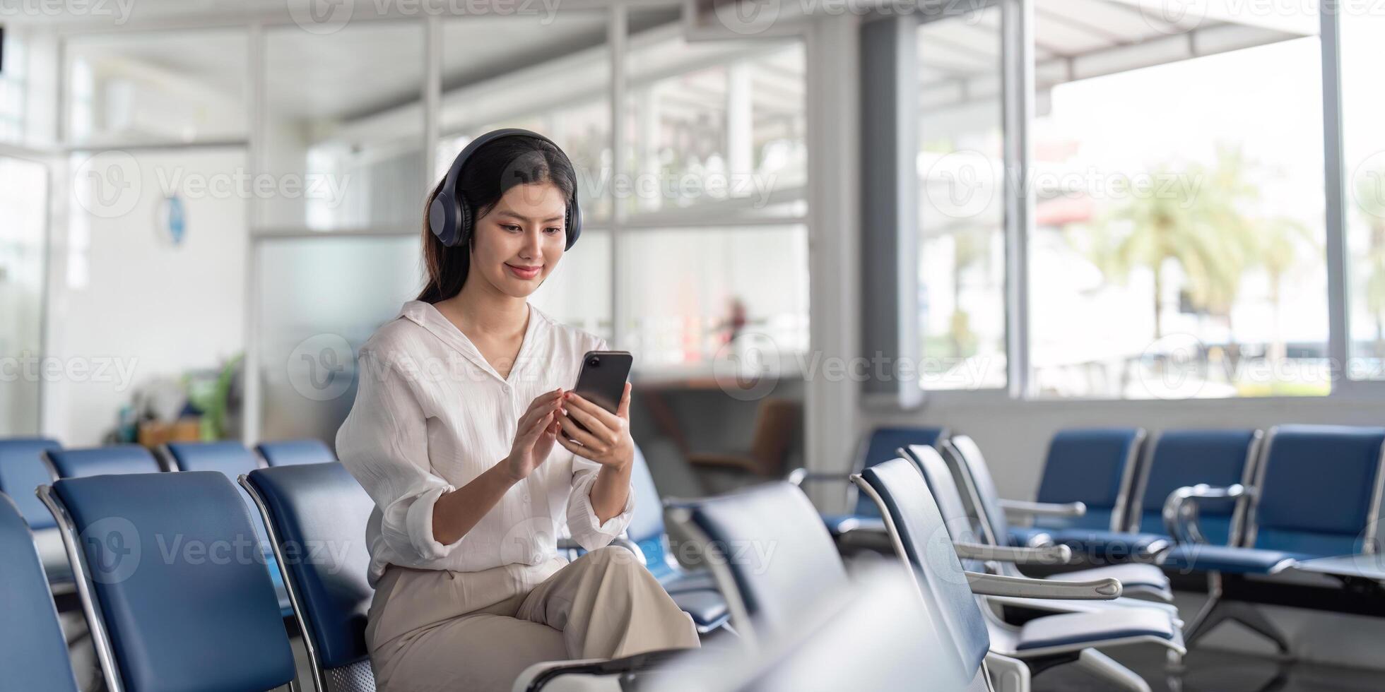 Happy young woman with headphones enjoying music while using smartphone in airport waiting area photo