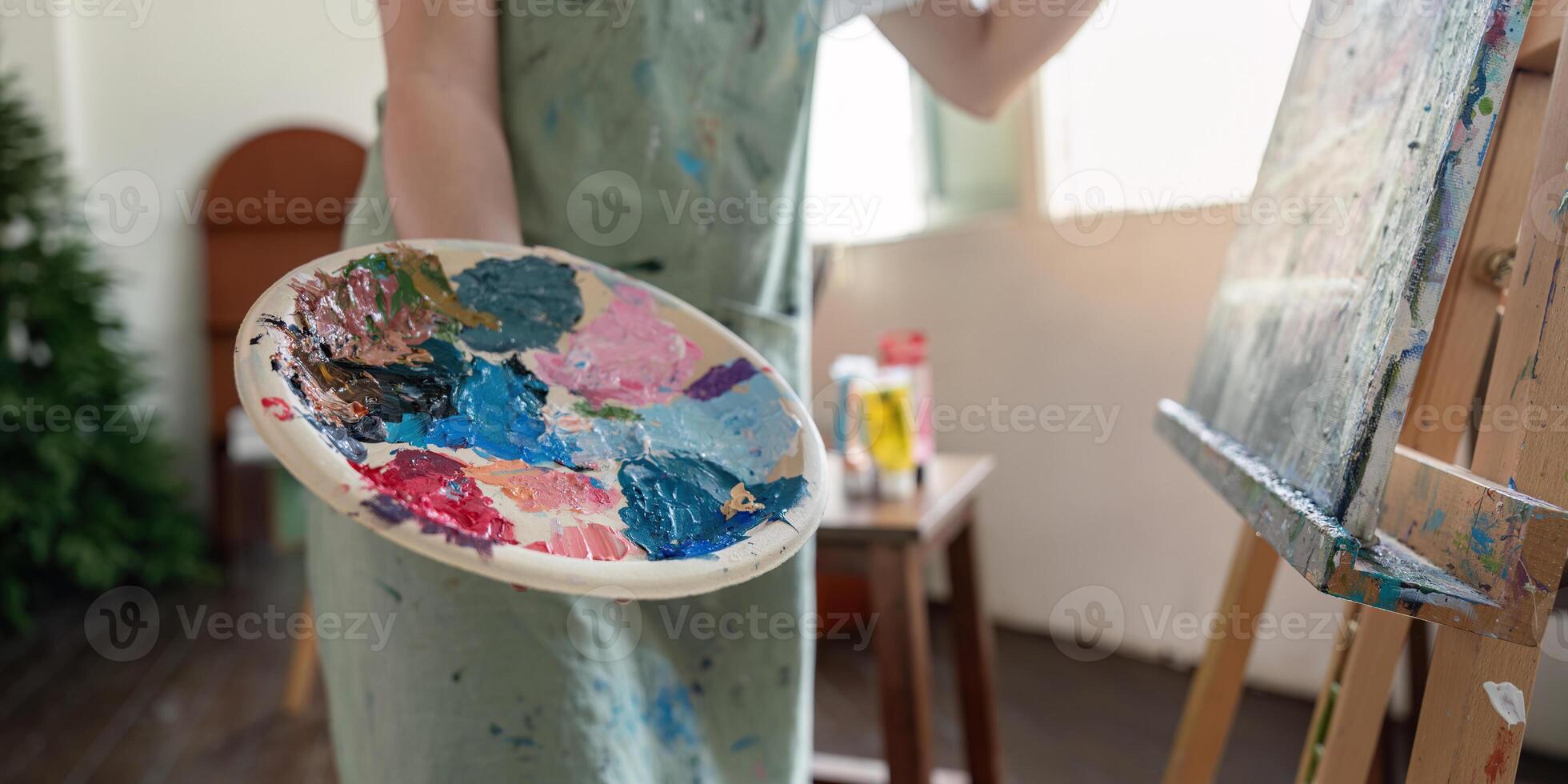 Focused artist presenting a colorful palette while preparing to paint on canvas in a light filled studio photo