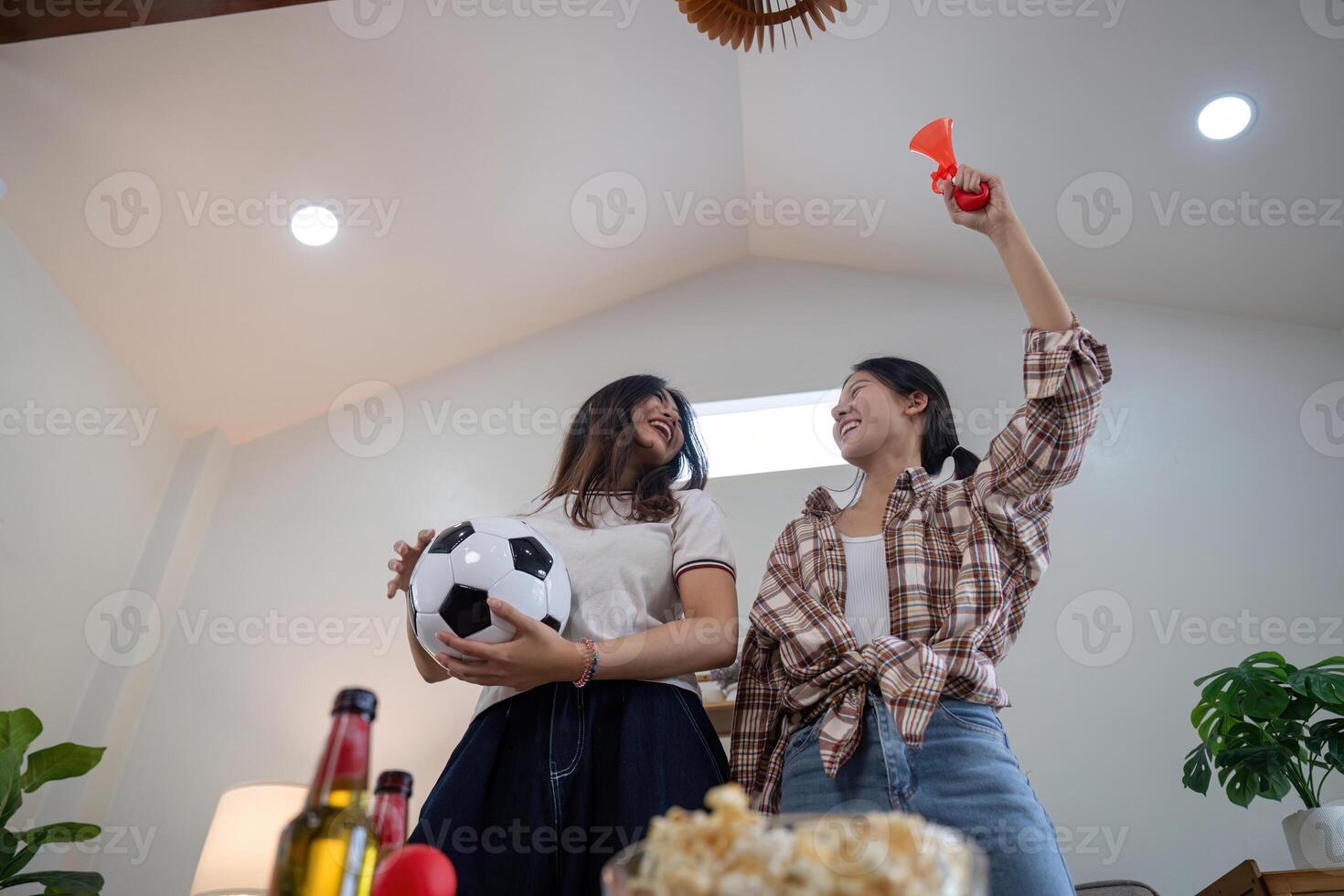 LGBT couple joyfully celebrating a soccer goal at home, holding snacks and cheering together photo