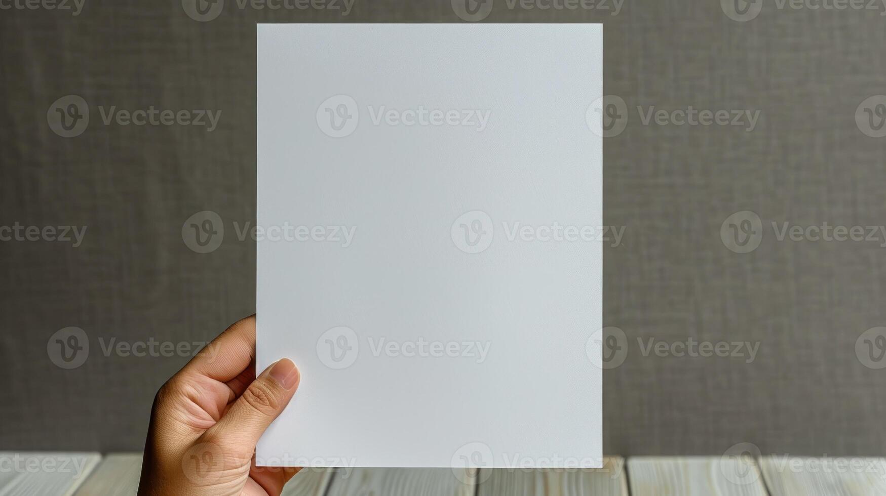 A hand holds a blank white sheet of paper against a textured gray backdrop photo