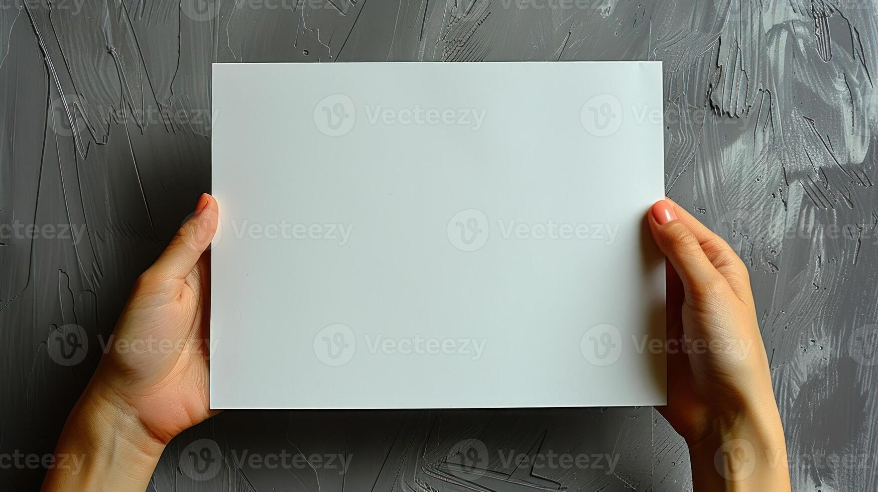 A person holds a blank white paper sheet in front of a grey concrete wall photo