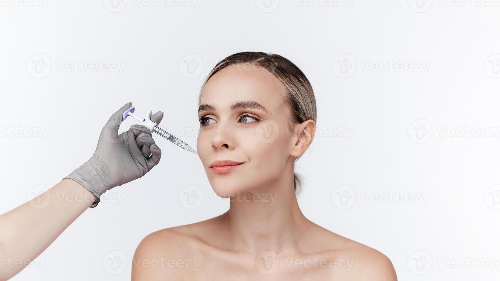 Closeup of young woman receiving hyaluronic acid injection isolated on white background. Beautician doing beauty procedure to female face with syringe, injection to her cheek. Cosmetology ads, banner photo
