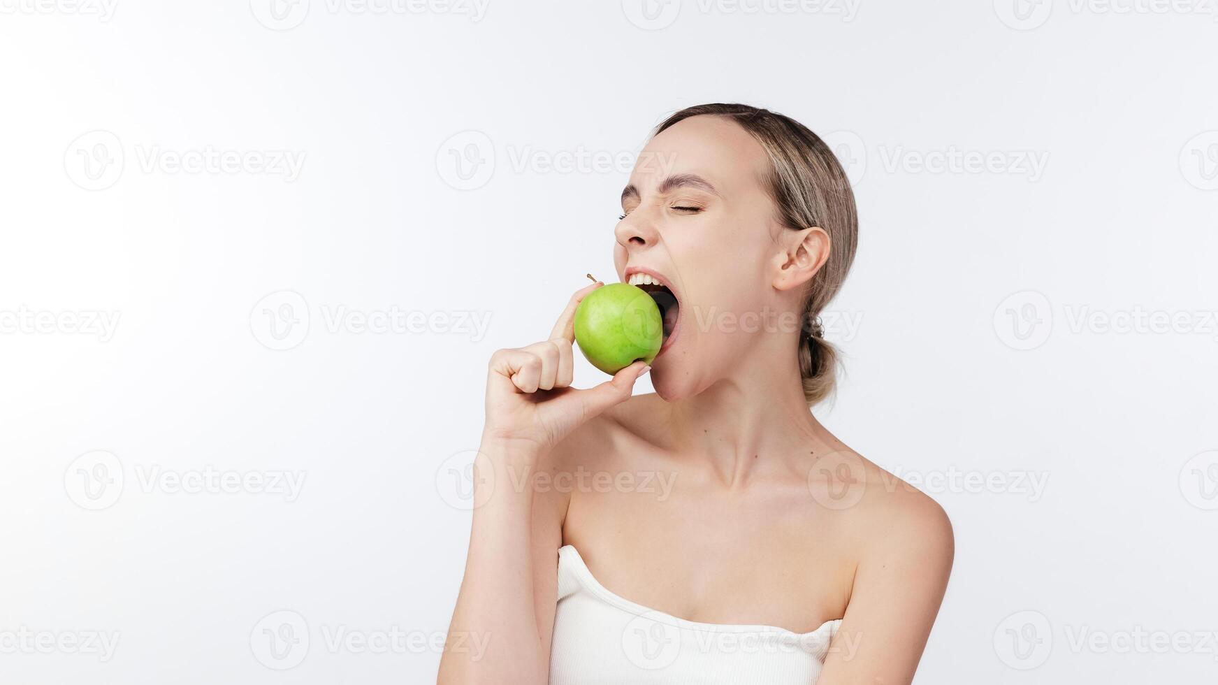 Happy woman biting Green Apple Posing Over White Background. Healthy nutrition, diet food Concept. Studio Shot, Isolated. Beauty health care lifestyle. Free copy space, banner. Stomatology concept. photo