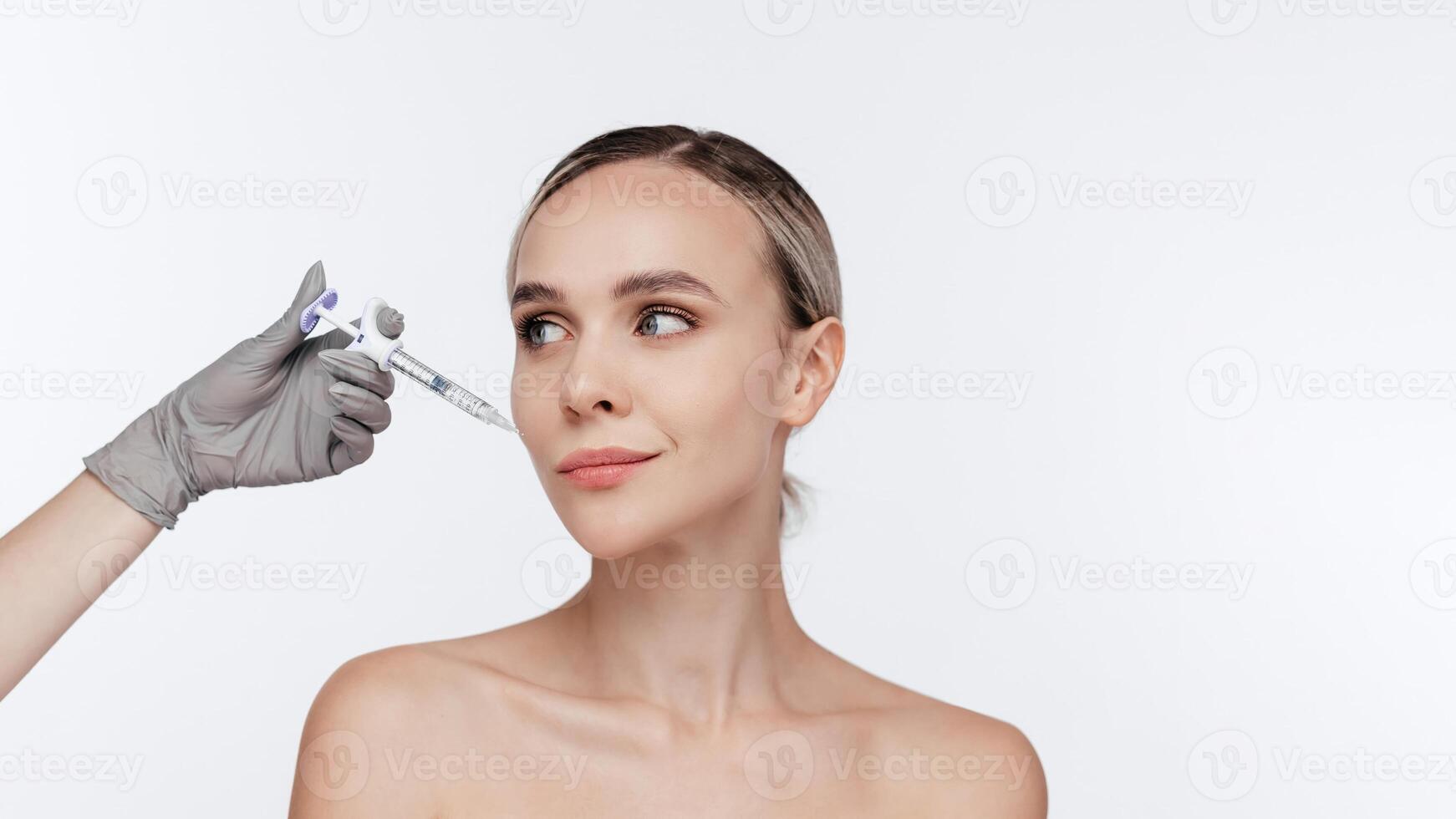 Blond woman receiving hyaluronic acid injection isolated on white background. Beautician doing beauty procedure to female face with syringe, injection to her cheek. Anti Aging Biorevitalization ads photo