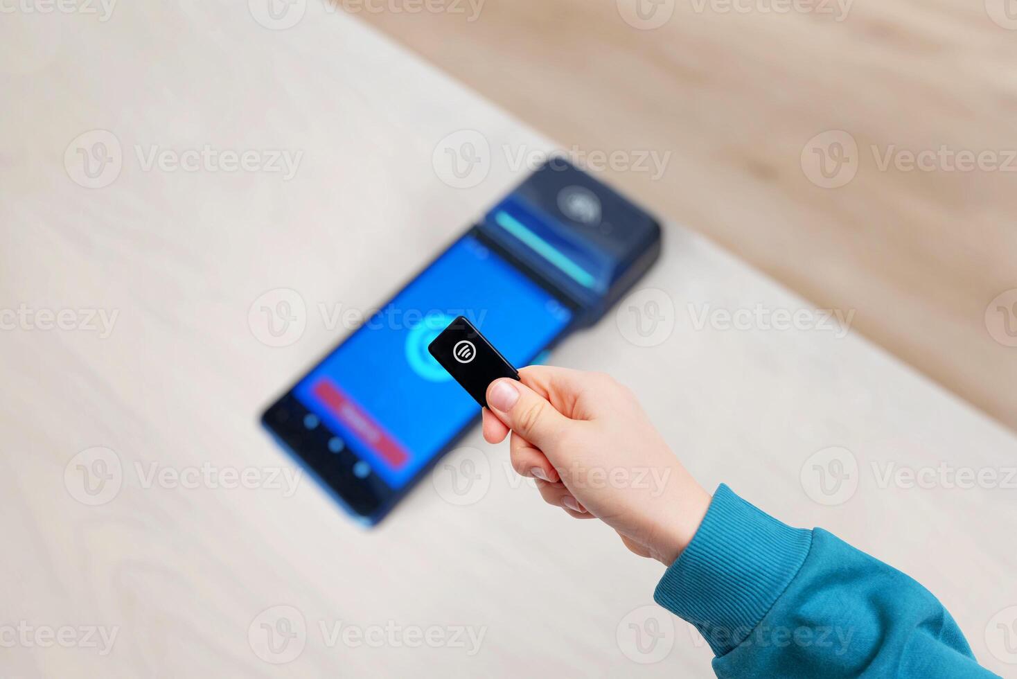 Small black key fob being used for payment on a POS terminal, held in a hand. A compact and modern contactless payment method photo