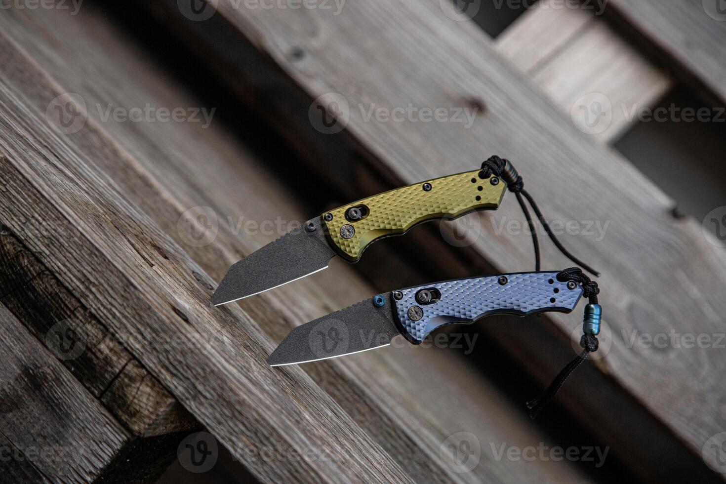 Two folding knives with textured handles, one green and one blue, are displayed on a rustic wooden surface photo
