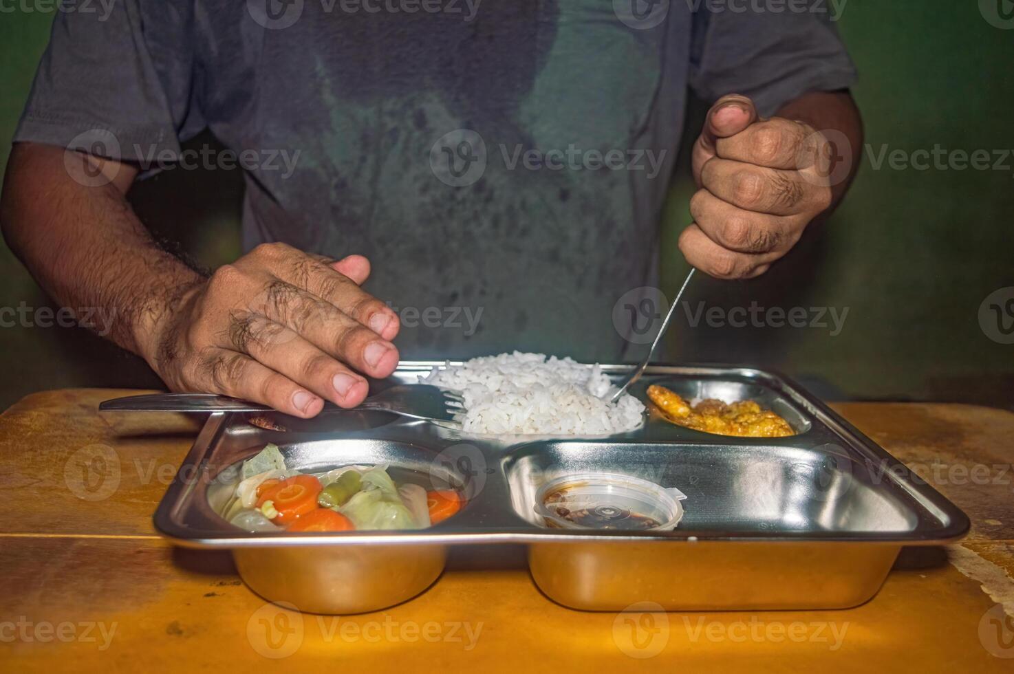 A person is eating a nutritious meal consisting of rice, vegetables, and fried food from a stainless steel tray, emphasizing the concept of a healthy and free lunch photo