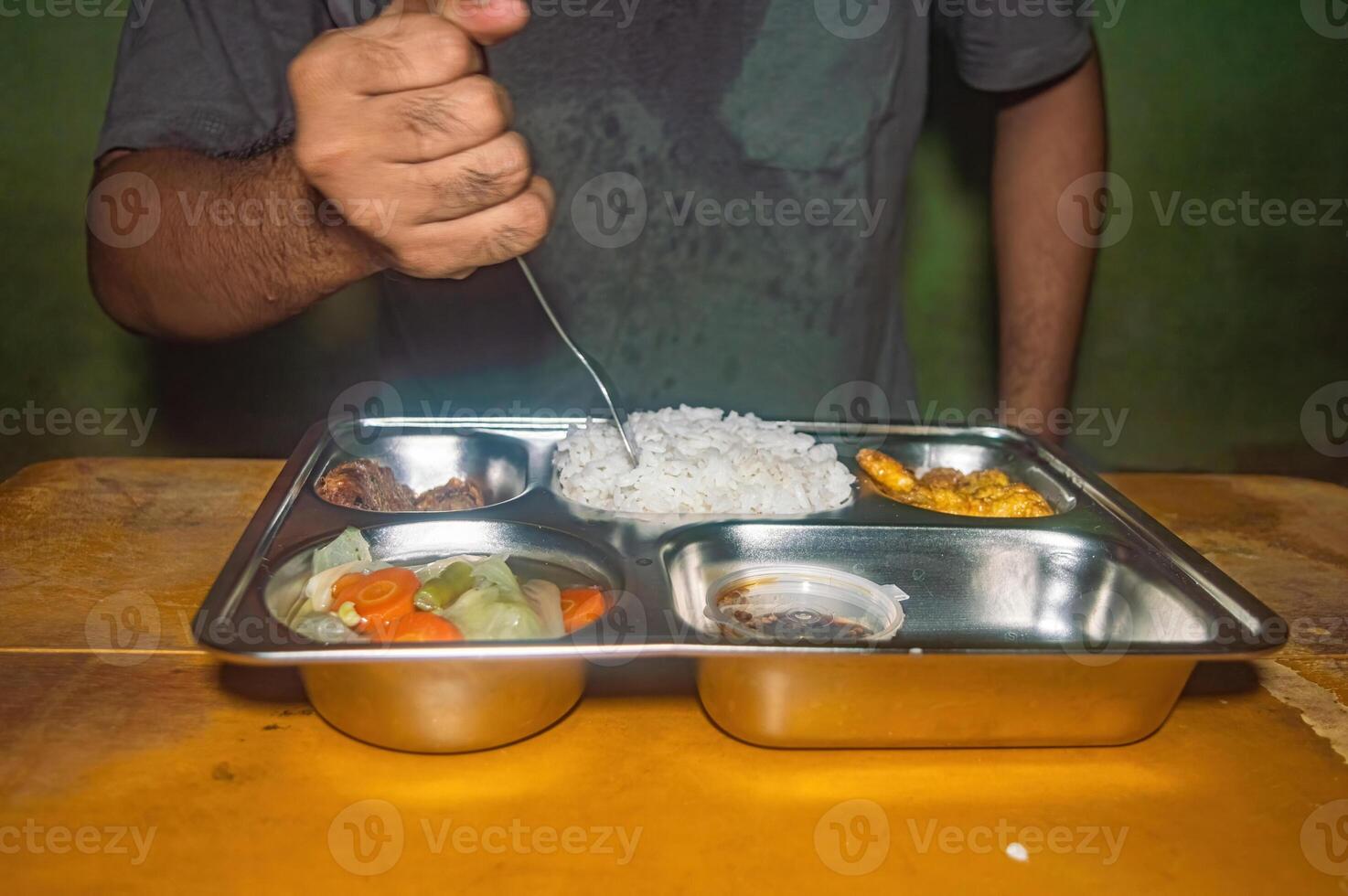 A person is having a nutritious and healthy free lunch consisting of rice, vegetables, and fried items on a stainless steel tray. The meal is balanced and visually appealing photo