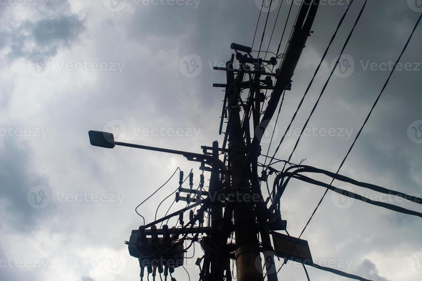 A silhouette of a utility pole with numerous wires and a streetlight against a cloudy sky, highlighting urban infrastructure photo