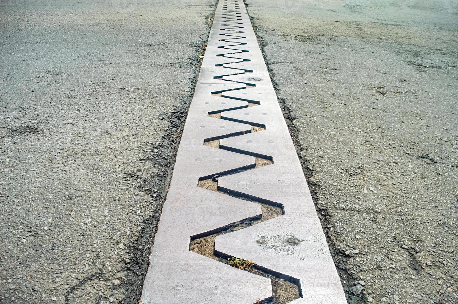 Close up of a bridge expansion joint with a zigzag pattern, designed to accommodate structural movements and prevent damage photo