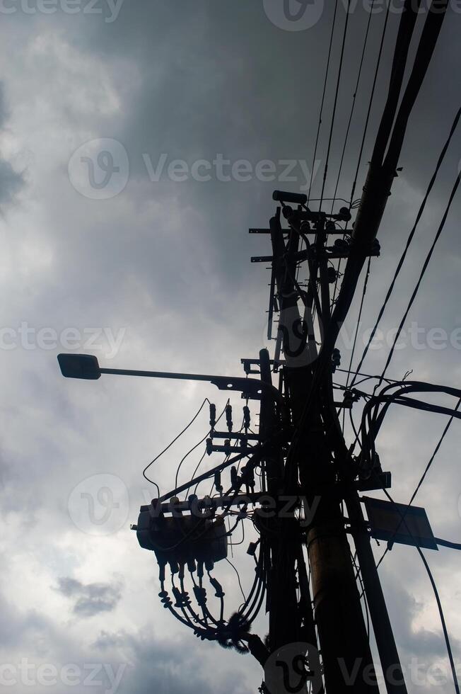 silhouette of a utility pole with numerous wires and a streetlight against a cloudy sky, highlighting urban infrastructure photo