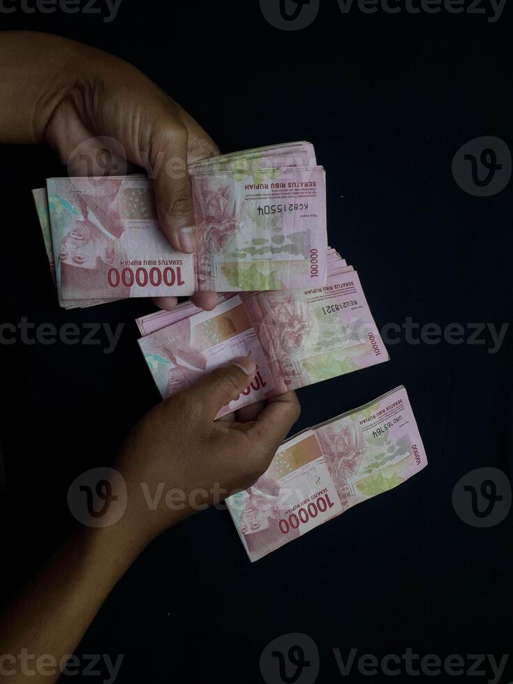 Hands holding stacks of one hundred thousand Indonesian Rupiah banknotes against black background photo