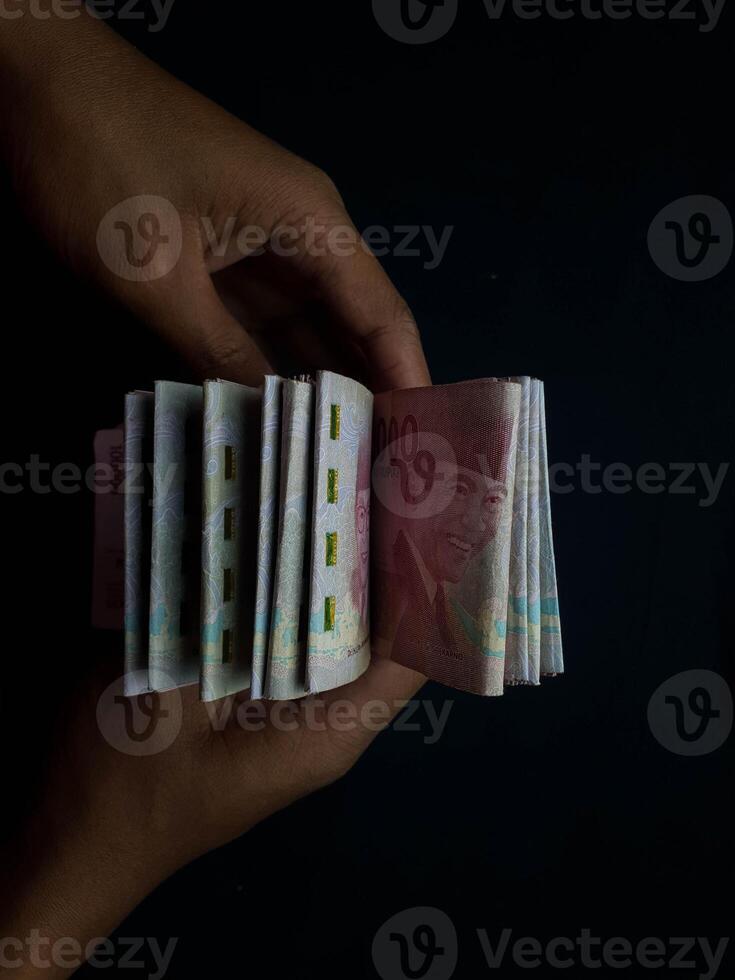 Hands holding a fanned stack of Indonesian Rupiah banknotes against a dark background photo