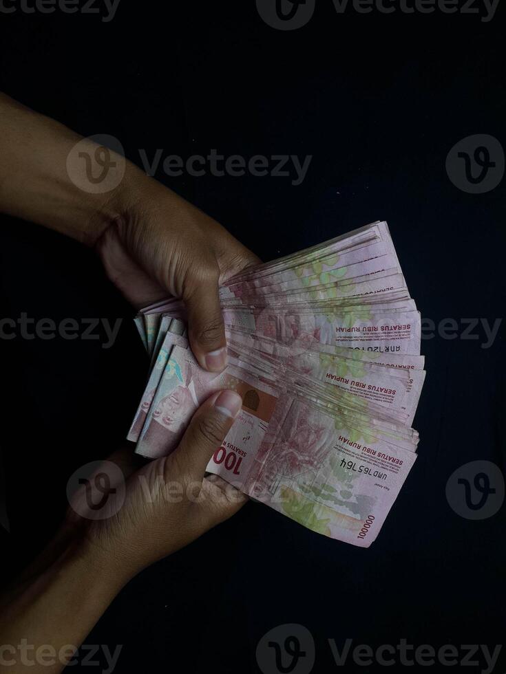 Hands holding a stack of Indonesian Rupiah banknotes against a dark backdrop photo