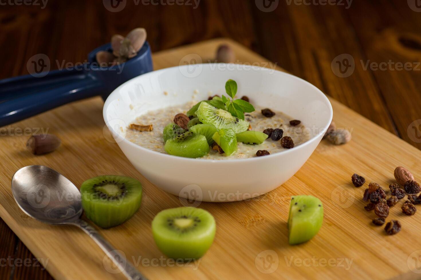 cooked oatmeal with kiwi, honey in a bowl on a wooden table photo